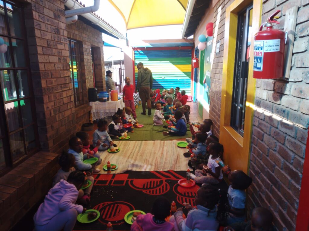 Kids at Tumishang day care enjoy their lunch with the help of Tshepo Sikosana 