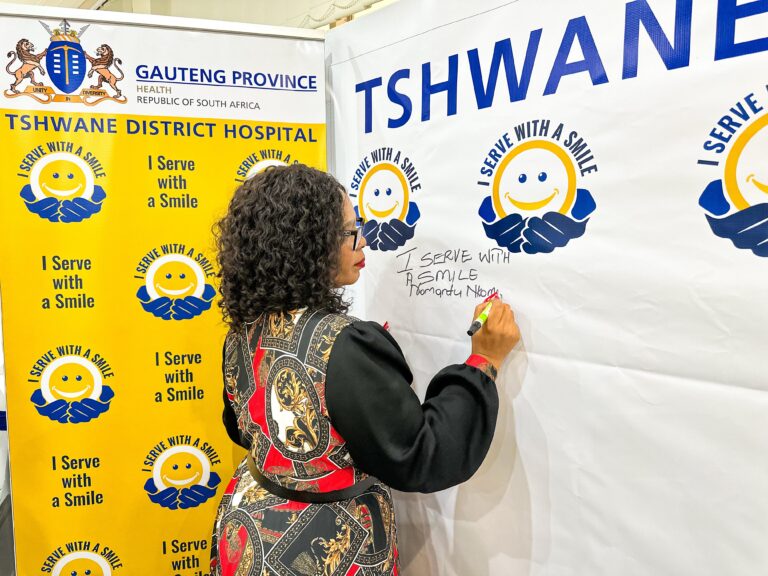 MEC for Health and wellness in Gauteng Nomantu Nkomo-Ralehoko, signing the "I serve with a smile" pledge, and an image of Health worker at Tshwane District Hospital explaining to MEC how one of the new X-Ray machines functions photo supplied